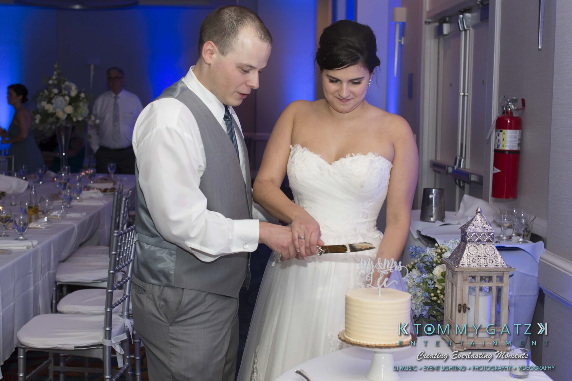Carly-Patrick-FINAL-Blog-Watermark-42 - TOMMY GATZ ENTERTAINMENT A bride and groom cut their wedding cake together in a decorated reception hall.
