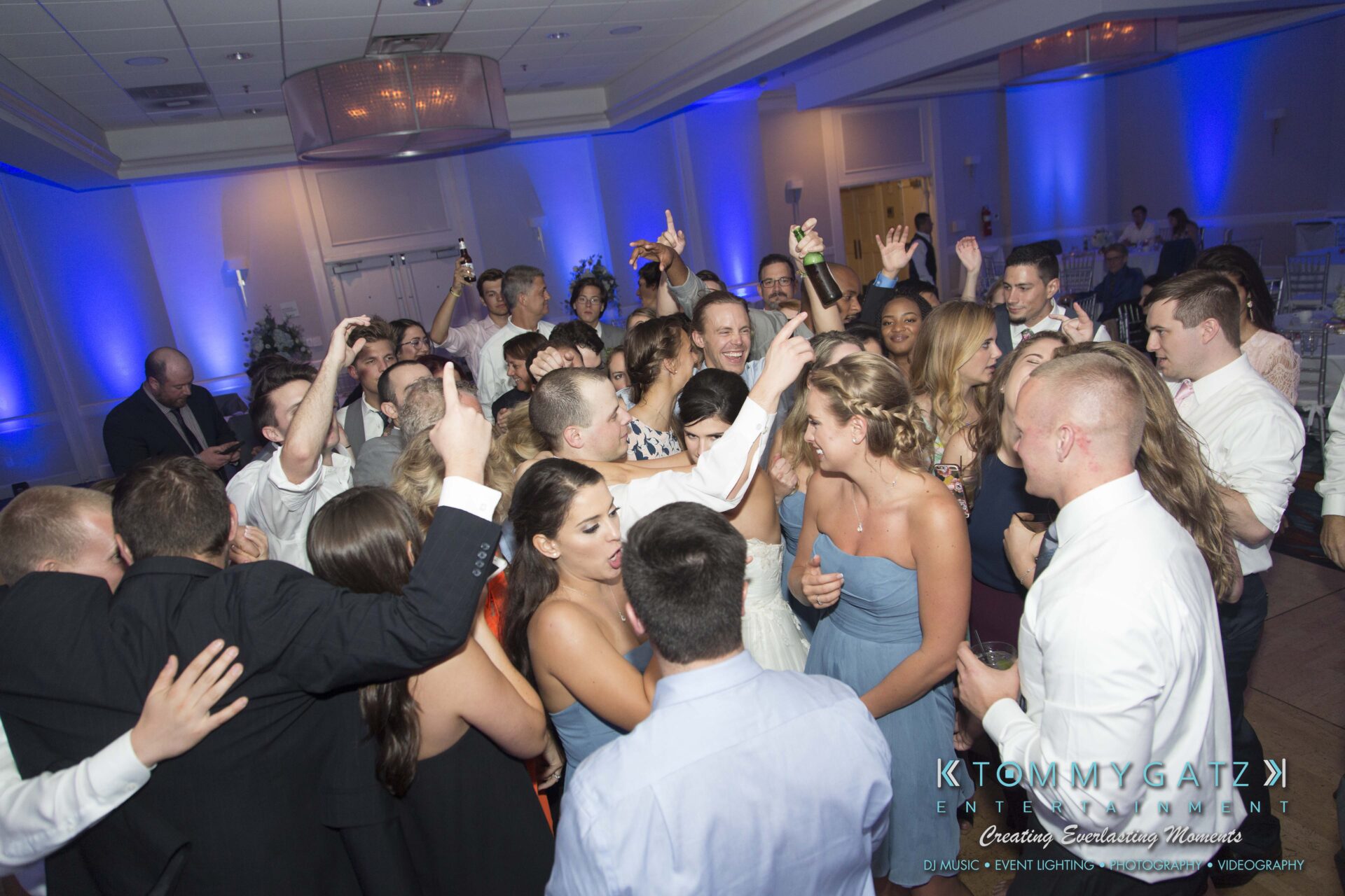 Carly-Patrick-FINAL-Blog-Watermark-53 - TOMMY GATZ ENTERTAINMENT A lively group of people dancing and celebrating at an indoor event, with blue lighting and formal attire.
