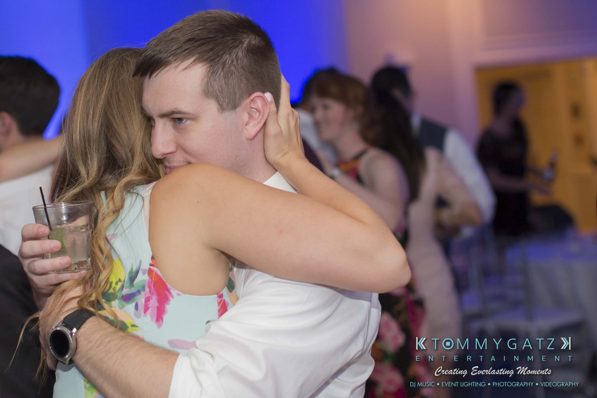 Carly-Patrick-FINAL-Blog-Watermark-55 - TOMMY GATZ ENTERTAINMENT A man and woman embrace while dancing at an event. The woman holds a drink, and other people are in the background.