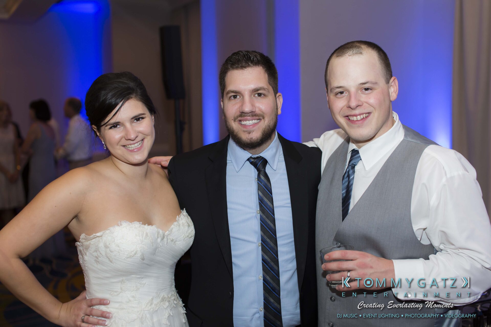 Carly-Patrick-FINAL-Blog-Watermark-57 - TOMMY GATZ ENTERTAINMENT Three people smiling at an event; one woman in a white dress and two men in suits.