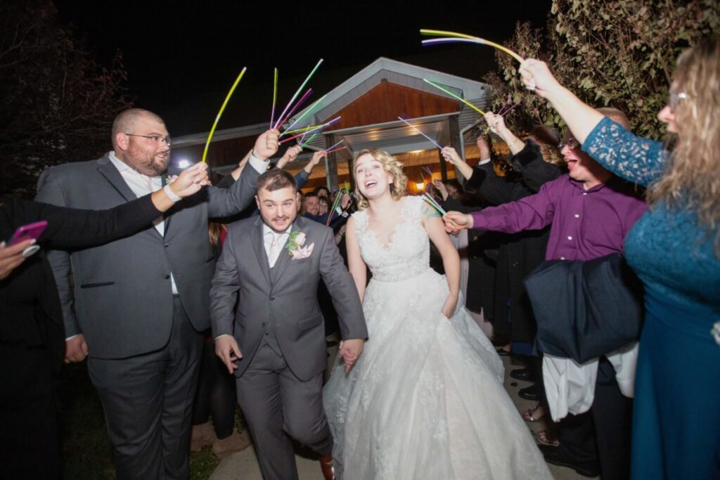 Christine-Jon-Wedding-Blog-103 - TOMMY GATZ ENTERTAINMENT Bride and groom walk through a crowd at night, holding glow sticks.