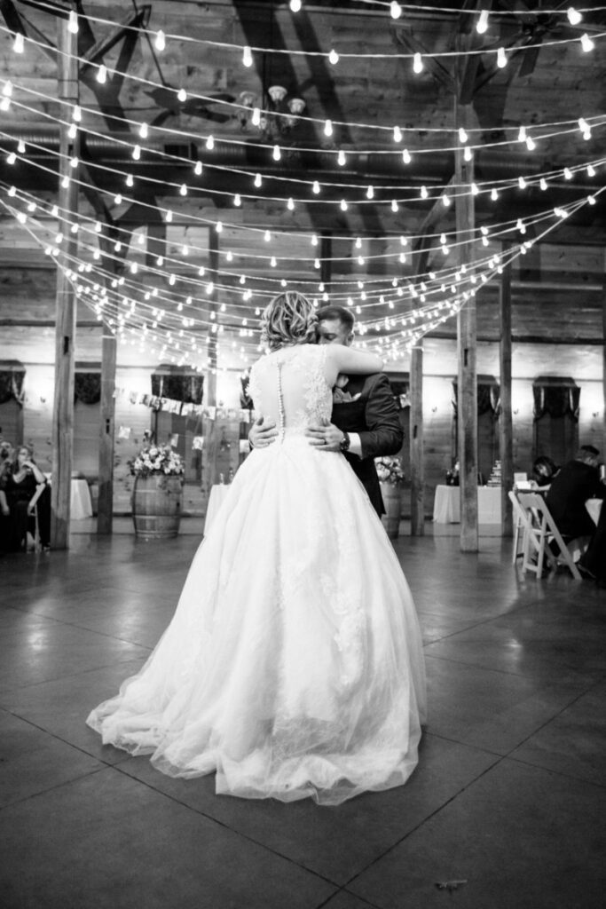 Christine-Jon-Wedding-Blog-97 - TOMMY GATZ ENTERTAINMENT A bride and groom share their first dance under string lights in a rustic venue.