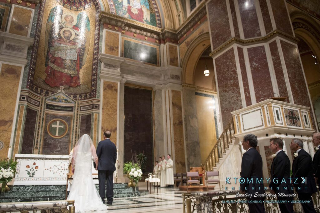 © alexandermorozovcom All Rights Reserved inquire by text +1-443-858-8743 - TOMMY GATZ ENTERTAINMENT Bride and groom standing at the altar in a large, ornate church as guests watch.