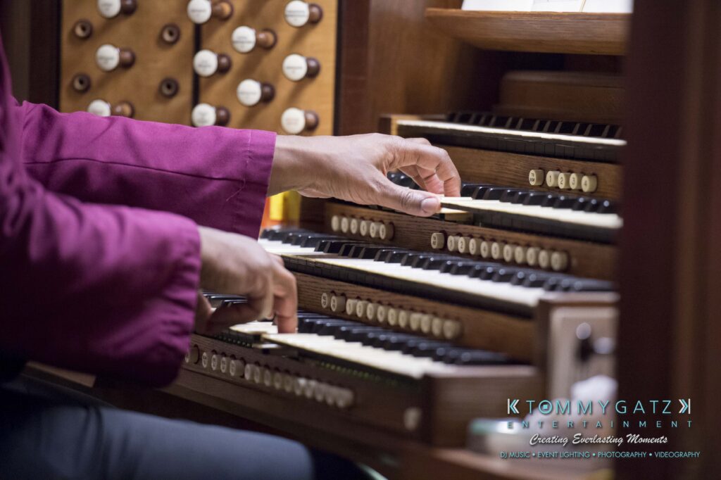 © alexandermorozovcom All Rights Reserved inquire by text +1-443-858-8743 - TOMMY GATZ ENTERTAINMENT Hands playing an organ with multiple keyboards and buttons, wearing a red sleeve.
