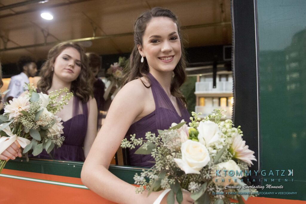 Elizabeth-Tom-101417-PREP-Low-Res-WM-147 - TOMMY GATZ ENTERTAINMENT Two women in purple dresses hold flower bouquets inside a vehicle.