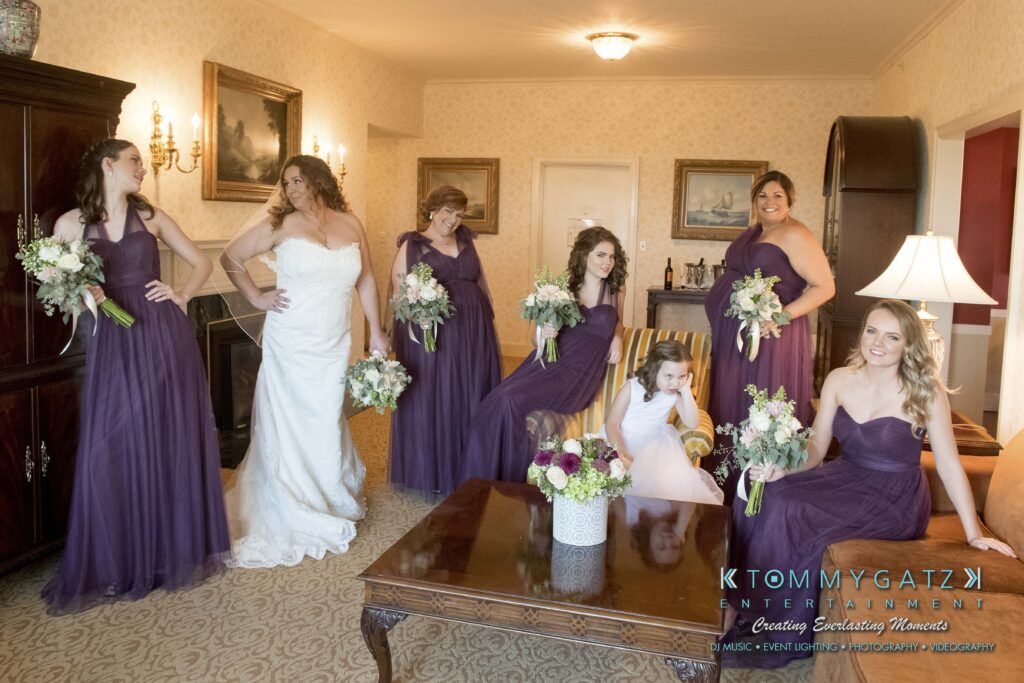 © alexandermorozovcom All Rights Reserved inquire by text +1-443-858-8743 - TOMMY GATZ ENTERTAINMENT Bride in white gown with bridesmaids in purple dresses holding bouquets, posed in a room with elegant decor.