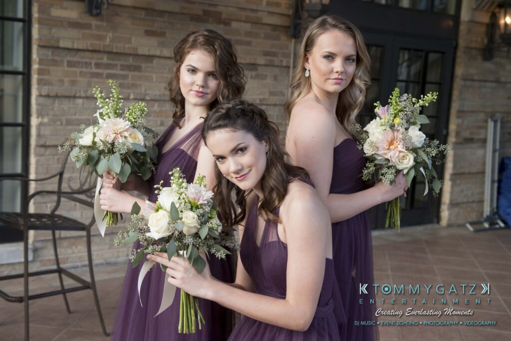 © alexandermorozovcom All Rights Reserved inquire by text +1-443-858-8743 - TOMMY GATZ ENTERTAINMENT Three women in purple dresses holding bouquets pose together indoors.