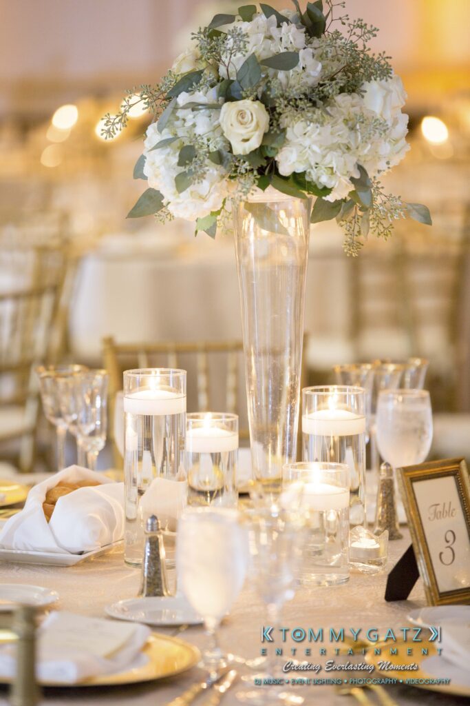 Elizabeth-Tom-101417-RECEPTION-Low-Res-WM-369 - TOMMY GATZ ENTERTAINMENT Elegant table setting with a tall floral centerpiece, candles in glass holders, and a table number card.