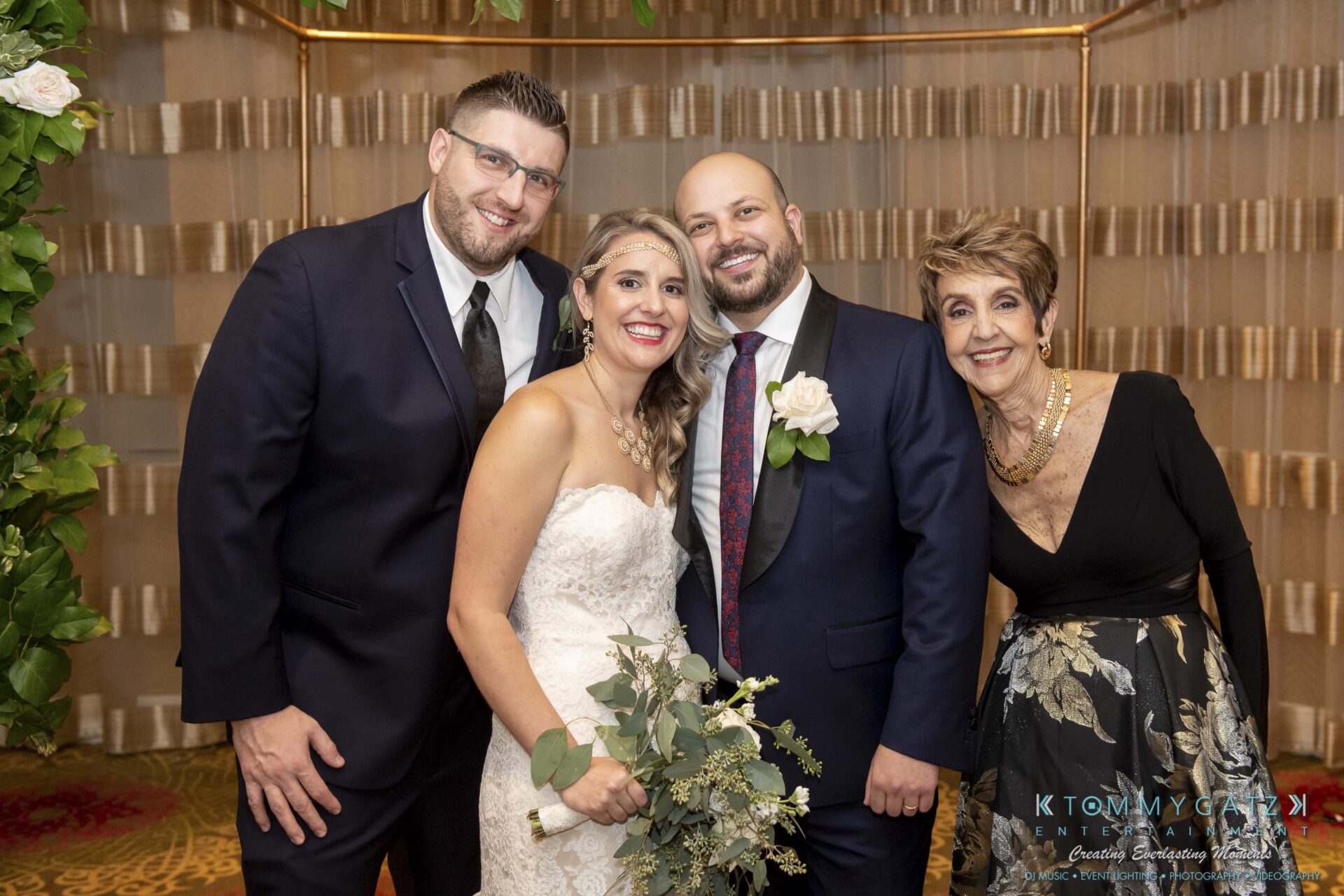 A bride and groom are standing with three guests at a wedding. The group is smiling and posing for the photo.