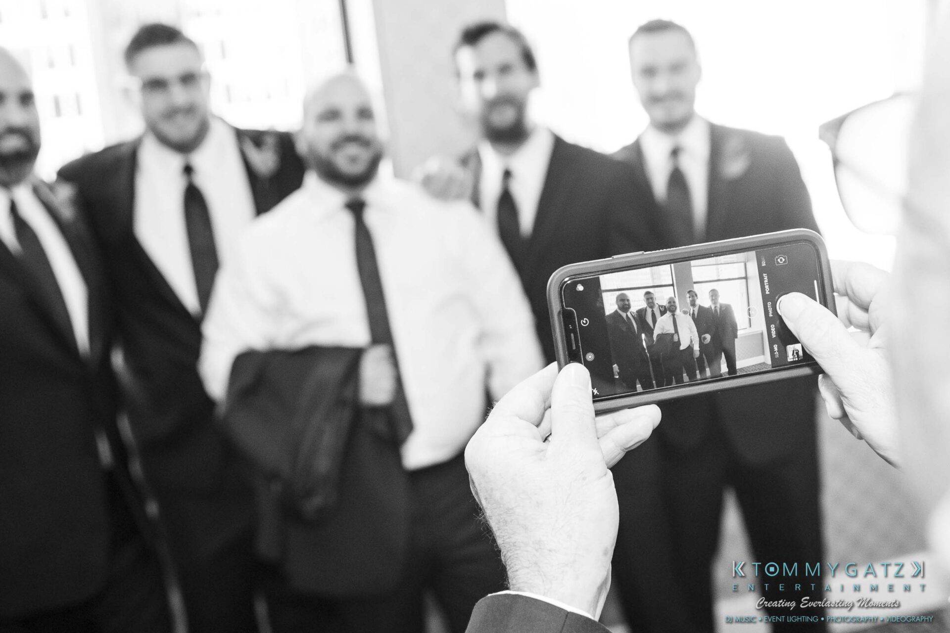 A person takes a photo of five men in suits using a smartphone.