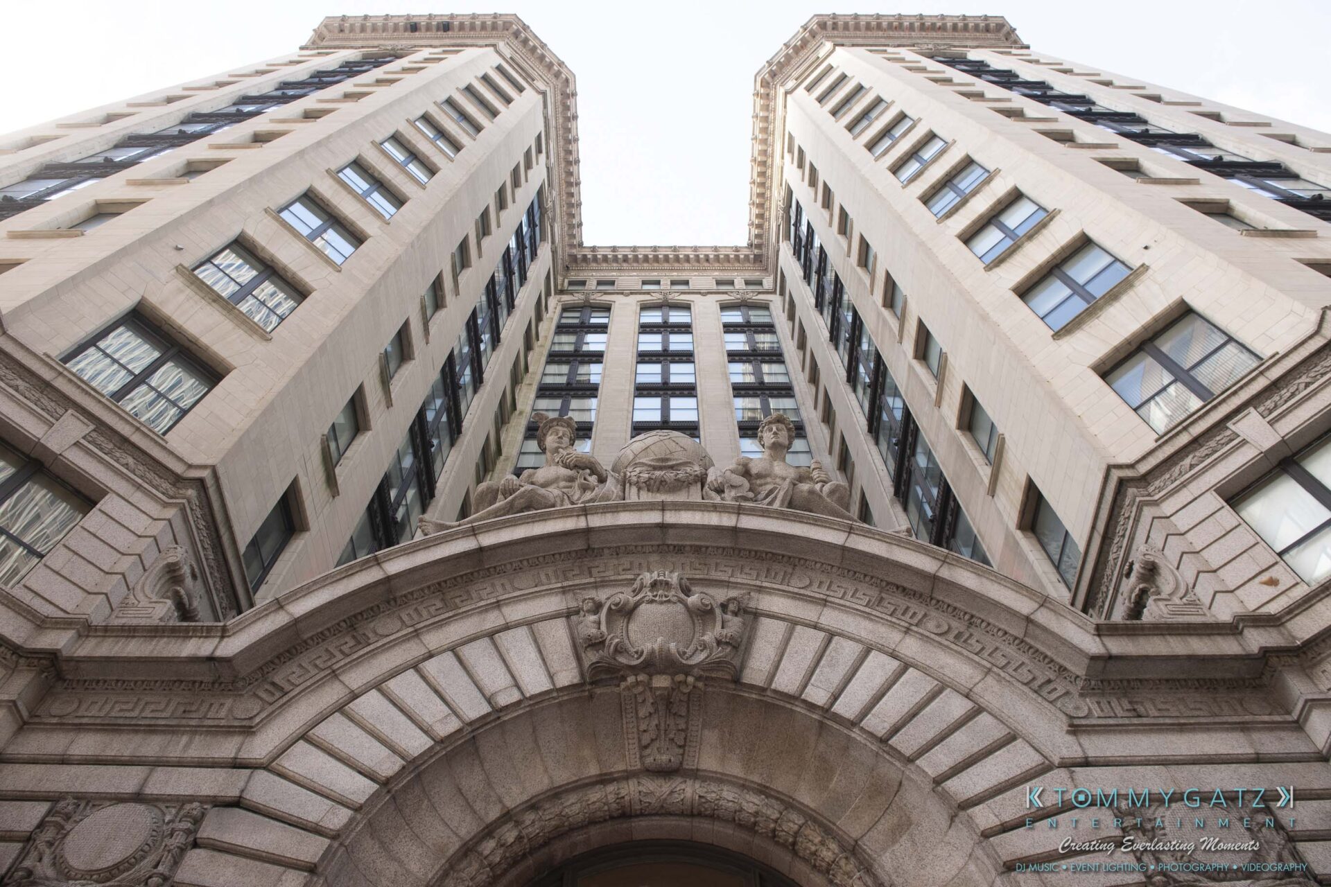 Upward view of a historic, ornate stone building with two symmetrical towers and intricate carvings above an arched entrance.