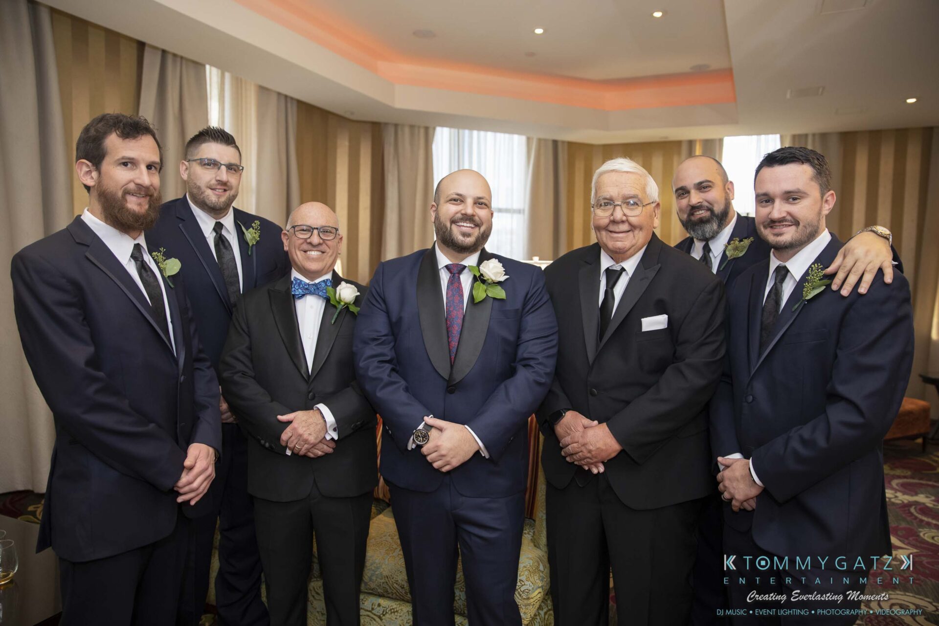 A group of seven men in formal attire posing together at an indoor event.