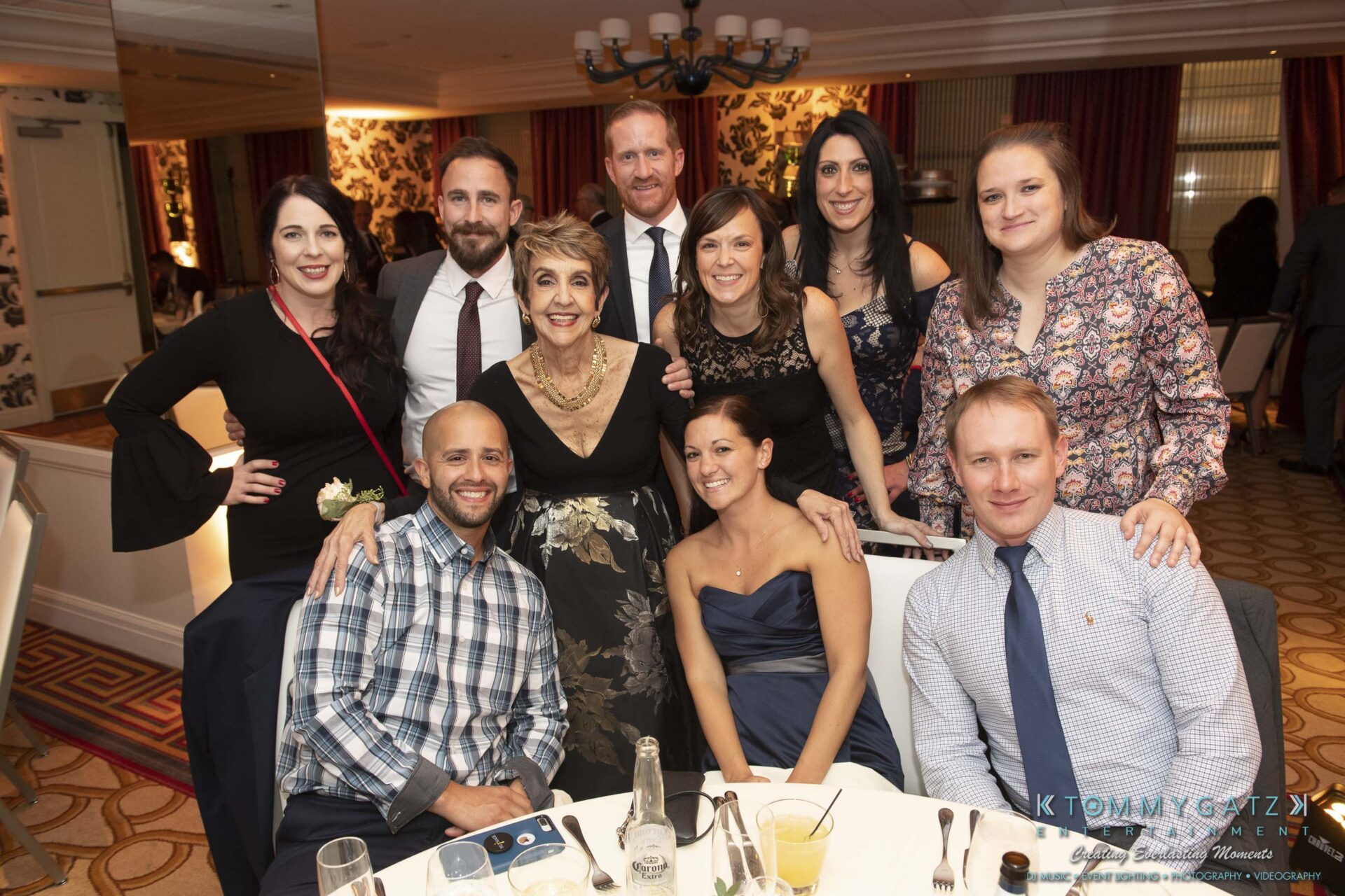 Group of people smiling at a formal event, with five standing and four seated around a table.