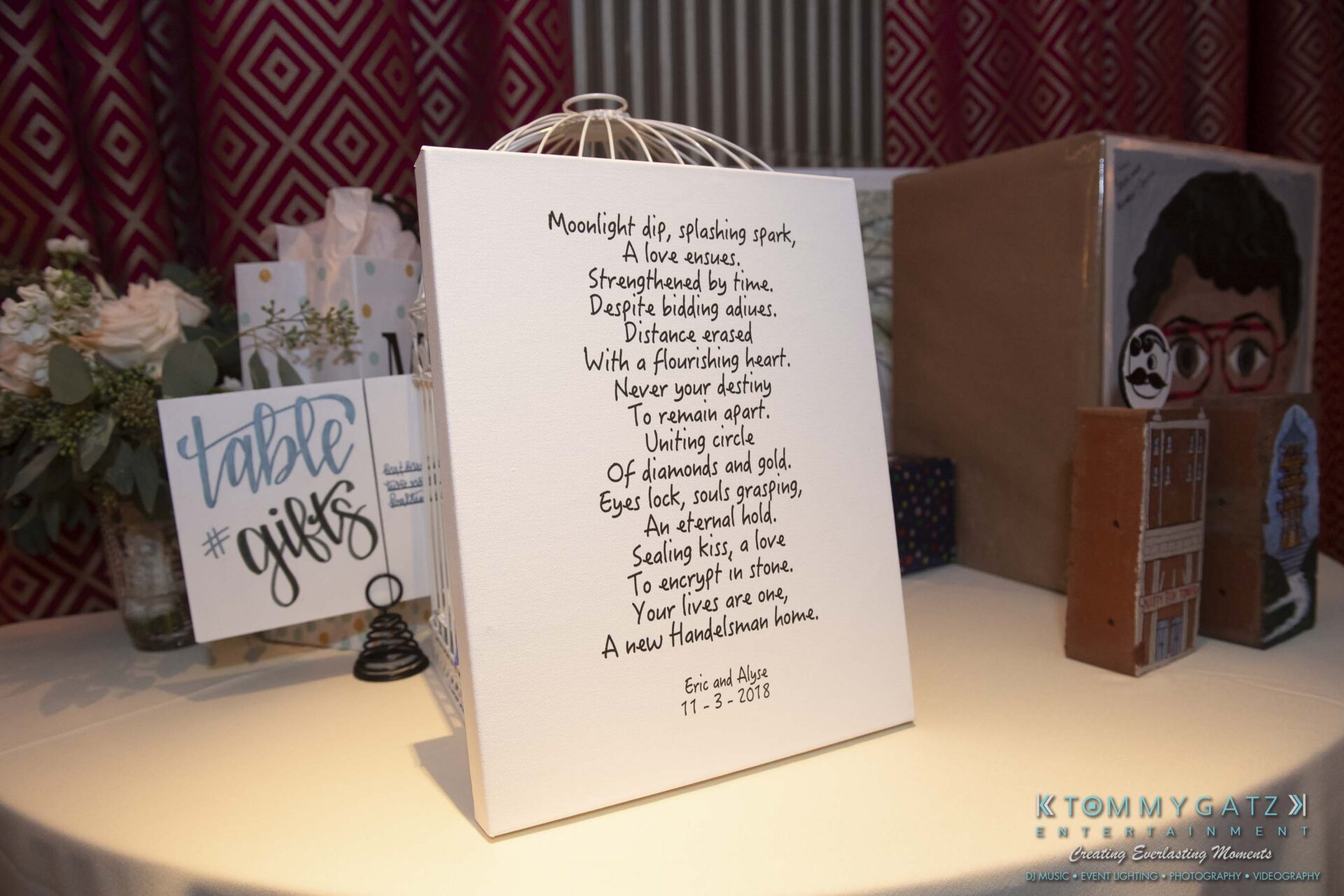 A decorative poem display stands on a table with gift boxes and a sign labeled "table gifts" nearby.