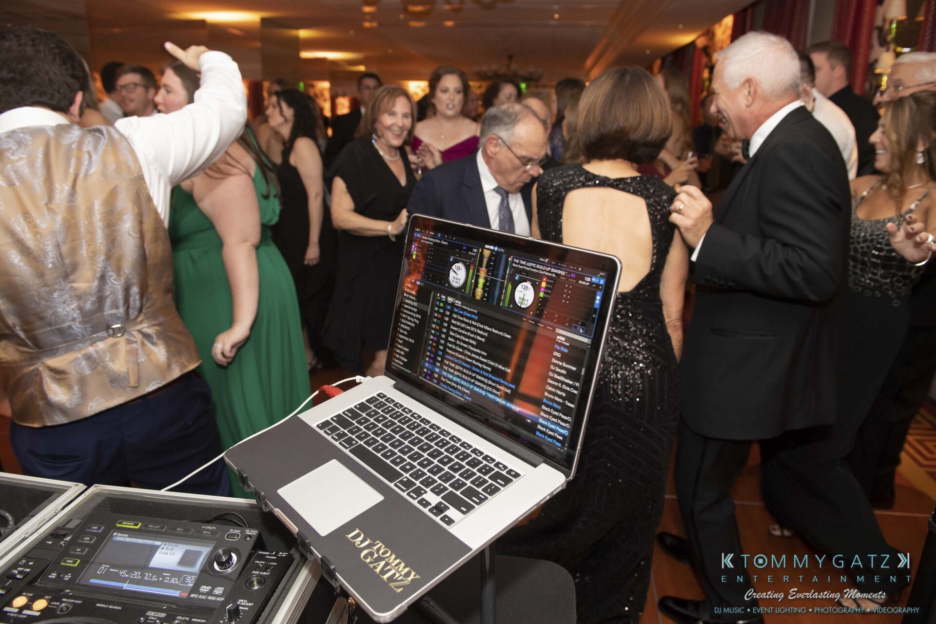 People dancing at an indoor event with a DJ booth in the foreground.