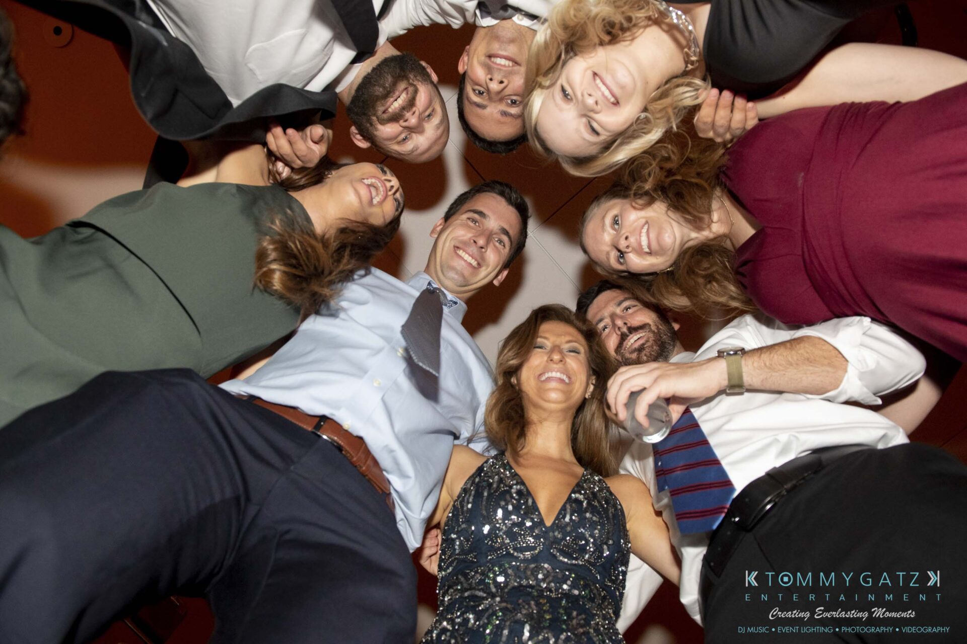 A group of people dressed in formal attire stand in a circle, smiling and looking down at the camera.