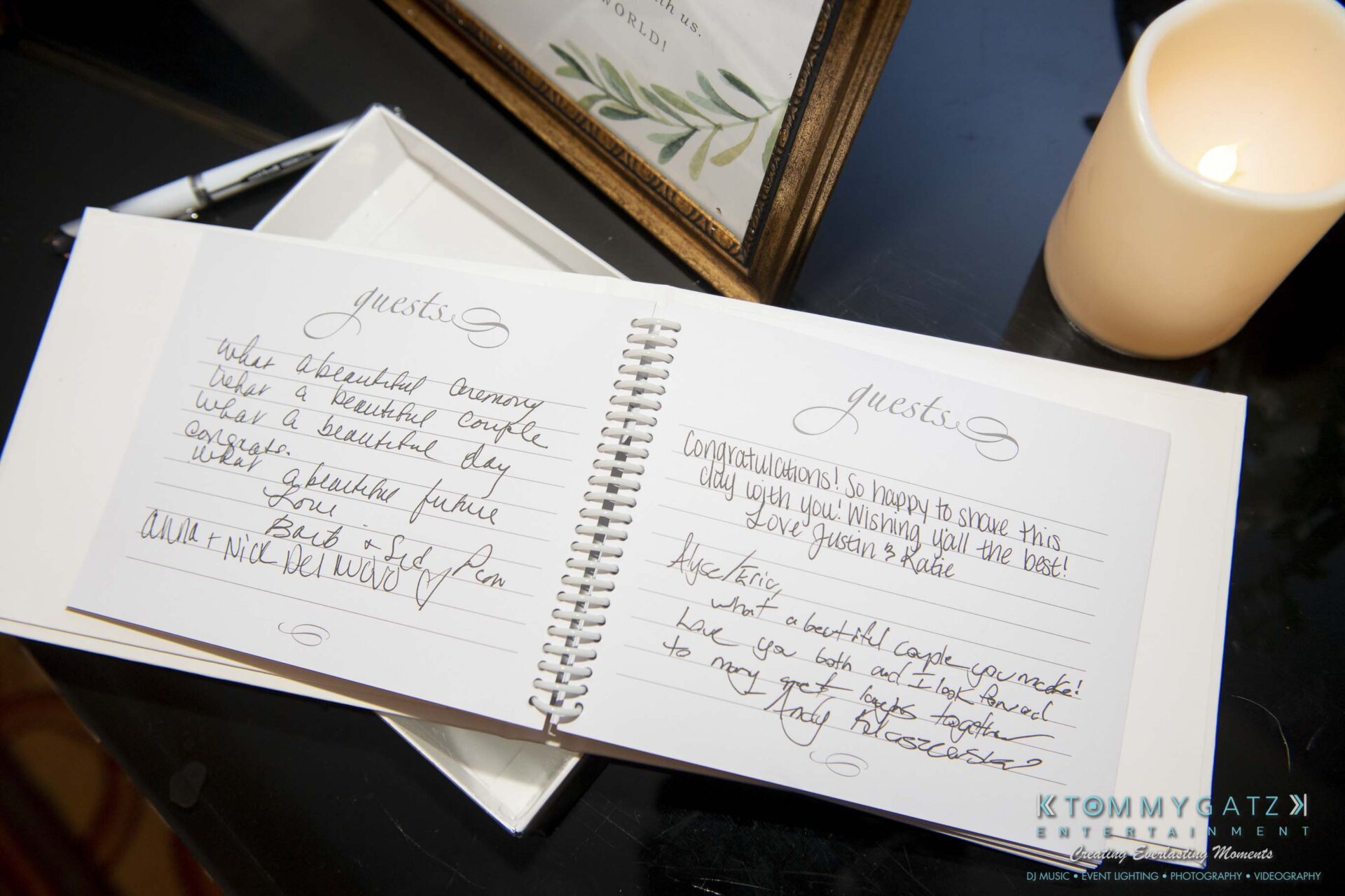 A guest book with handwritten messages, placed open on a table beside a lit candle and a sign in the background.