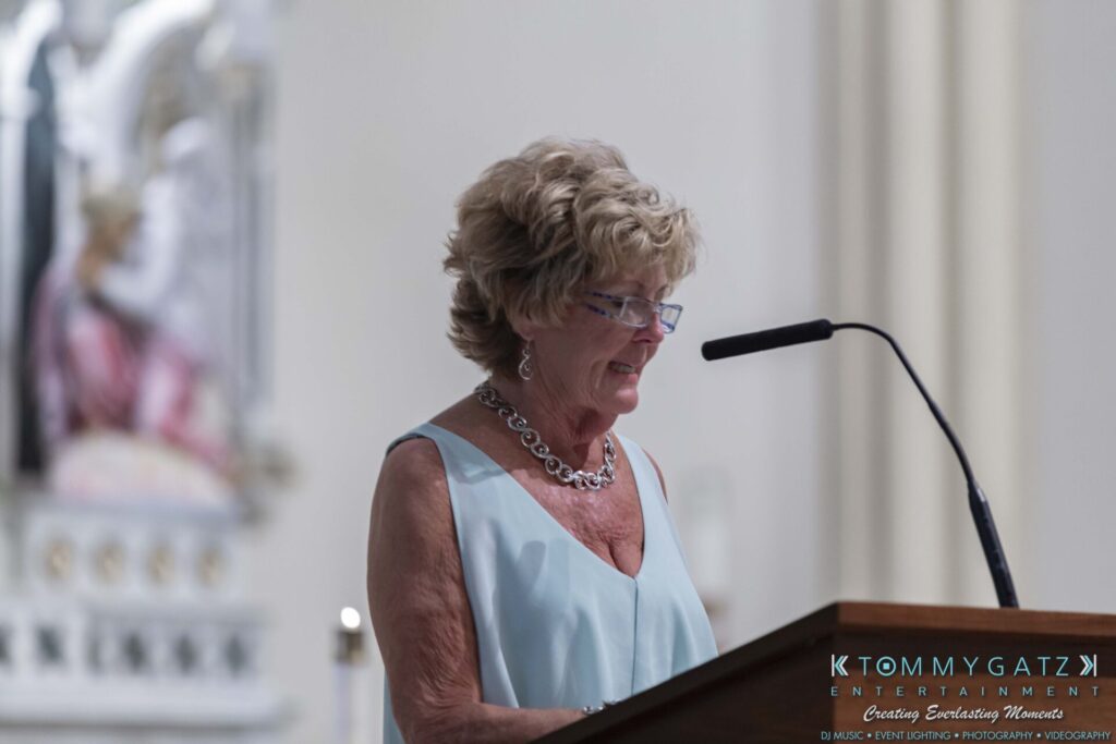 A person with short hair and glasses speaks at a podium with a microphone.