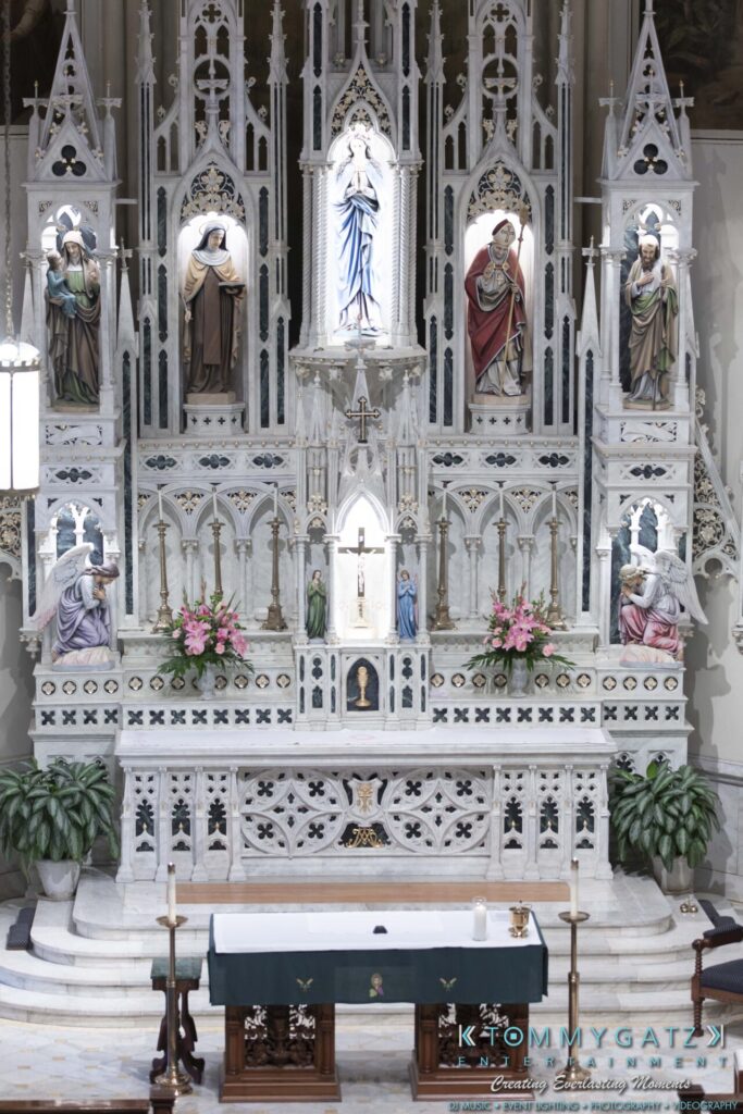 Grace-Michael-063018-PREP-Low-Res-WM-22 - TOMMY GATZ ENTERTAINMENT A detailed church altar with religious statues, ornate carvings, and floral arrangements.