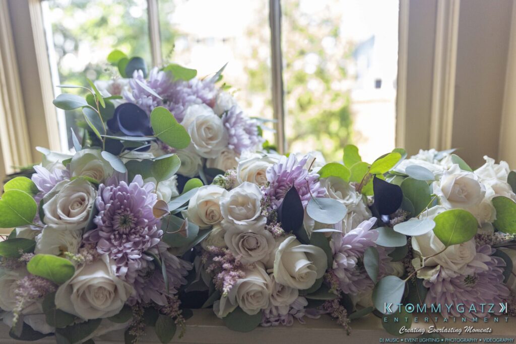 Grace-Michael-063018-PREP-Low-Res-WM-38 - TOMMY GATZ ENTERTAINMENT A collection of floral bouquets with white roses, purple flowers, and green leaves placed on a window ledge.
