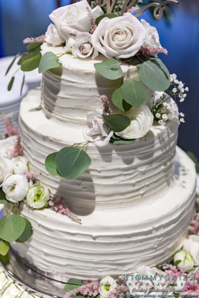 Three-tiered white wedding cake adorned with roses, greenery, and delicate flowers.