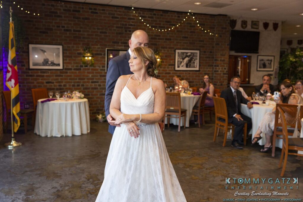 Grace-Michael-063018-RECEPTION-Low-Res-WM-395 - TOMMY GATZ ENTERTAINMENT A bride and groom dance in a brick-walled room decorated for a wedding reception, with guests seated at tables in the background.
