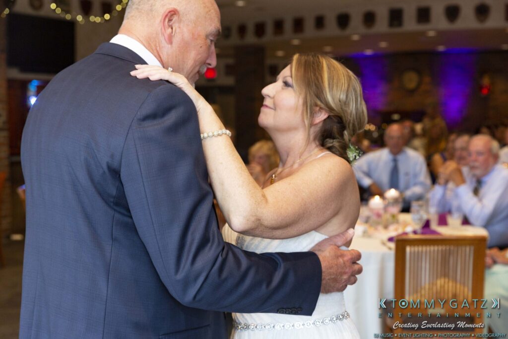 Grace-Michael-063018-RECEPTION-Low-Res-WM-397 - TOMMY GATZ ENTERTAINMENT An older couple dancing closely at a wedding reception, surrounded by seated guests in a decorated venue.