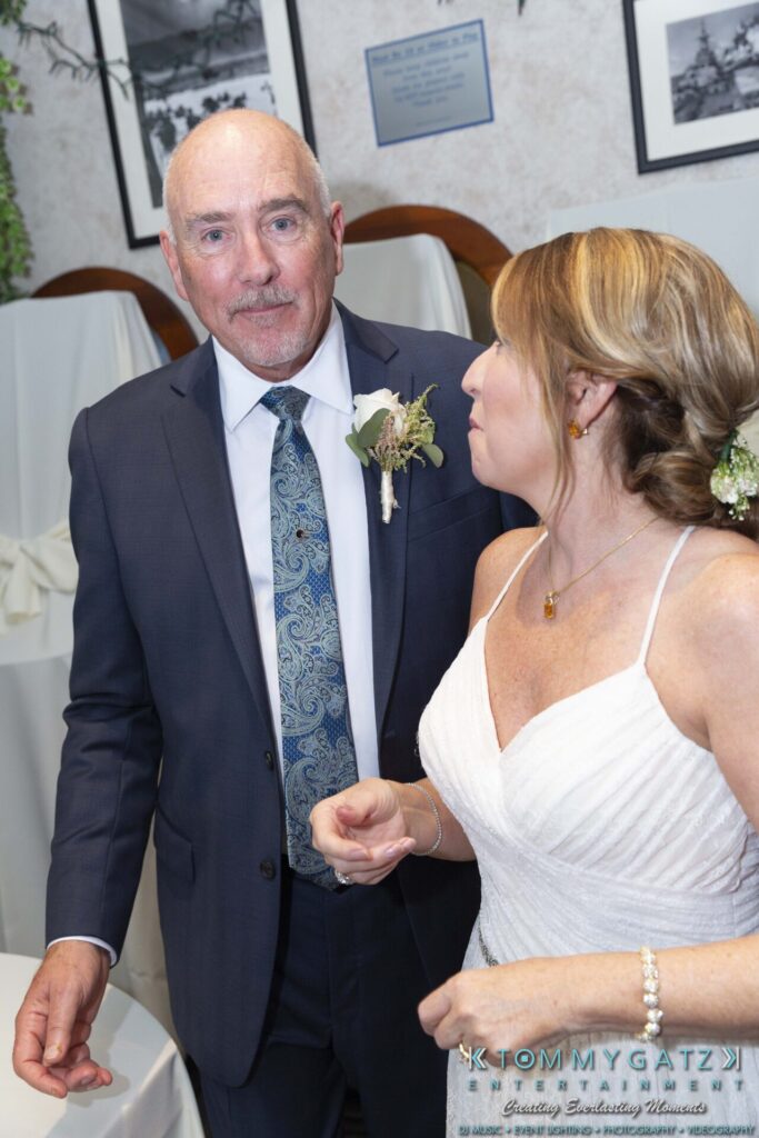 Grace-Michael-063018-RECEPTION-Low-Res-WM-421 - TOMMY GATZ ENTERTAINMENT A couple wearing formal attire, with the woman in a white gown and the man in a suit and tie, stand closely together in an indoor setting.