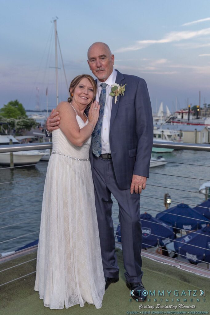 Grace-Michael-063018-RECEPTION-Low-Res-WM-504 - TOMMY GATZ ENTERTAINMENT A couple in wedding attire poses on a dock with boats and water in the background.