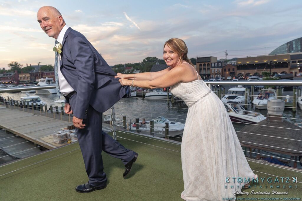 Grace-Michael-063018-RECEPTION-Low-Res-WM-513 - TOMMY GATZ ENTERTAINMENT A bride playfully pulls on the groom's suit jacket by a marina with boats in the background.