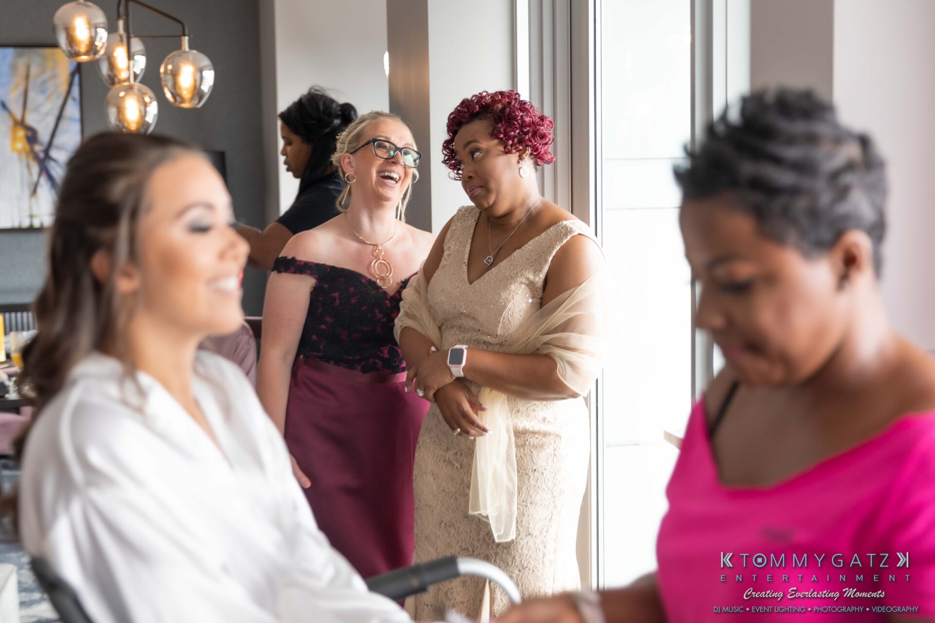 Harris-Wedding-HIGHLIGHTS-090119-10 - TOMMY GATZ ENTERTAINMENT Two women in formal dresses watch another woman getting ready, while a fourth woman assists. The setting appears to be a preparation area, possibly for an event.