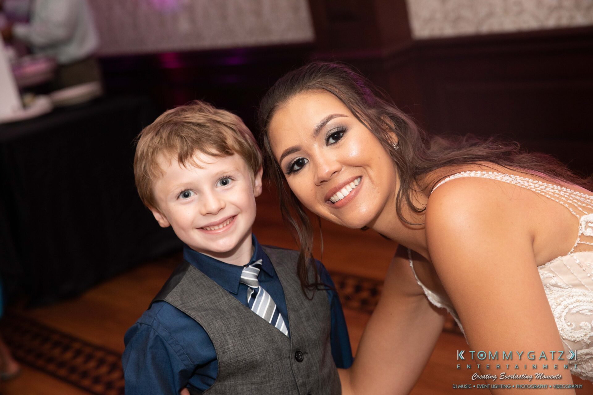 Harris-Wedding-HIGHLIGHTS-090119-111 - TOMMY GATZ ENTERTAINMENT A woman in a white dress and a young boy in a blue shirt and gray vest with a tie smile at the camera in a decorated indoor setting.