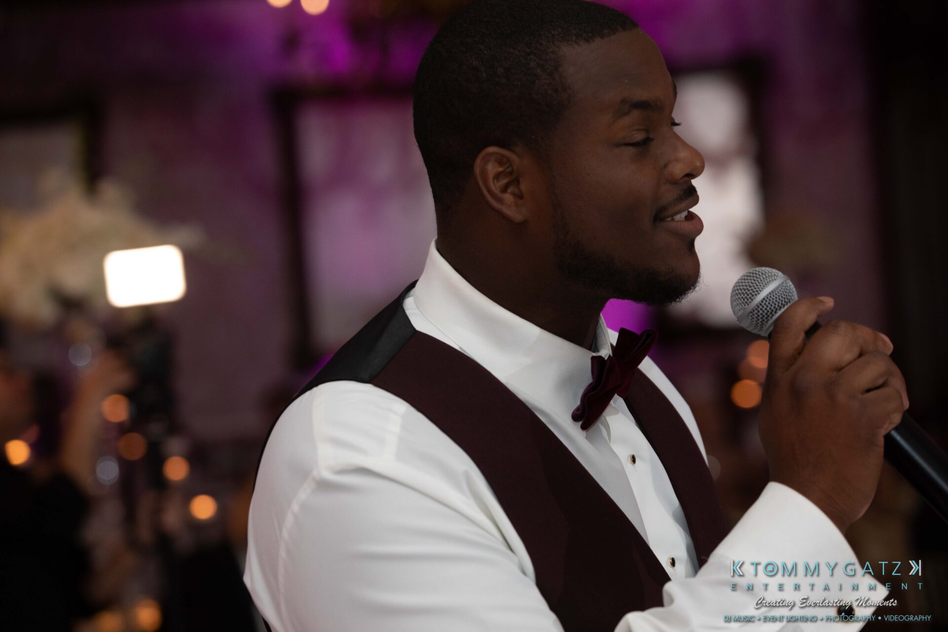 Harris-Wedding-HIGHLIGHTS-090119-115 - TOMMY GATZ ENTERTAINMENT A man in a tuxedo sings into a microphone at an indoor event with dim lighting.