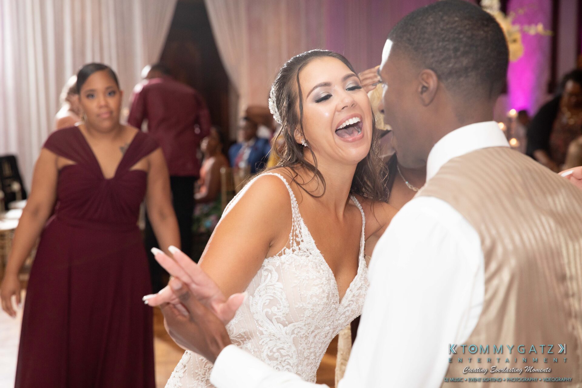 Harris-Wedding-HIGHLIGHTS-090119-119 - TOMMY GATZ ENTERTAINMENT Bride joyfully dancing with a man in a suit at a wedding reception, with guests in the background.