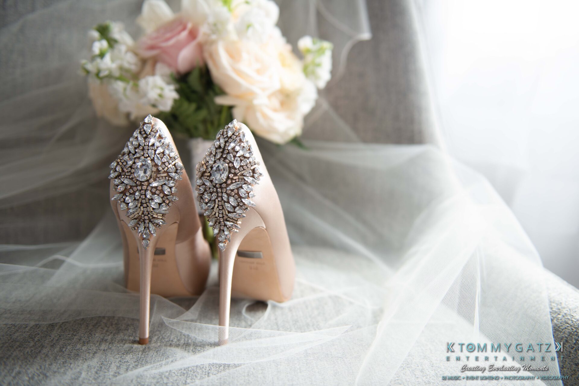 Harris-Wedding-HIGHLIGHTS-090119-3 - TOMMY GATZ ENTERTAINMENT Elegant high-heeled shoes with intricate jeweled patterns on the heels, placed on a chair with a bouquet of pale flowers in the background.