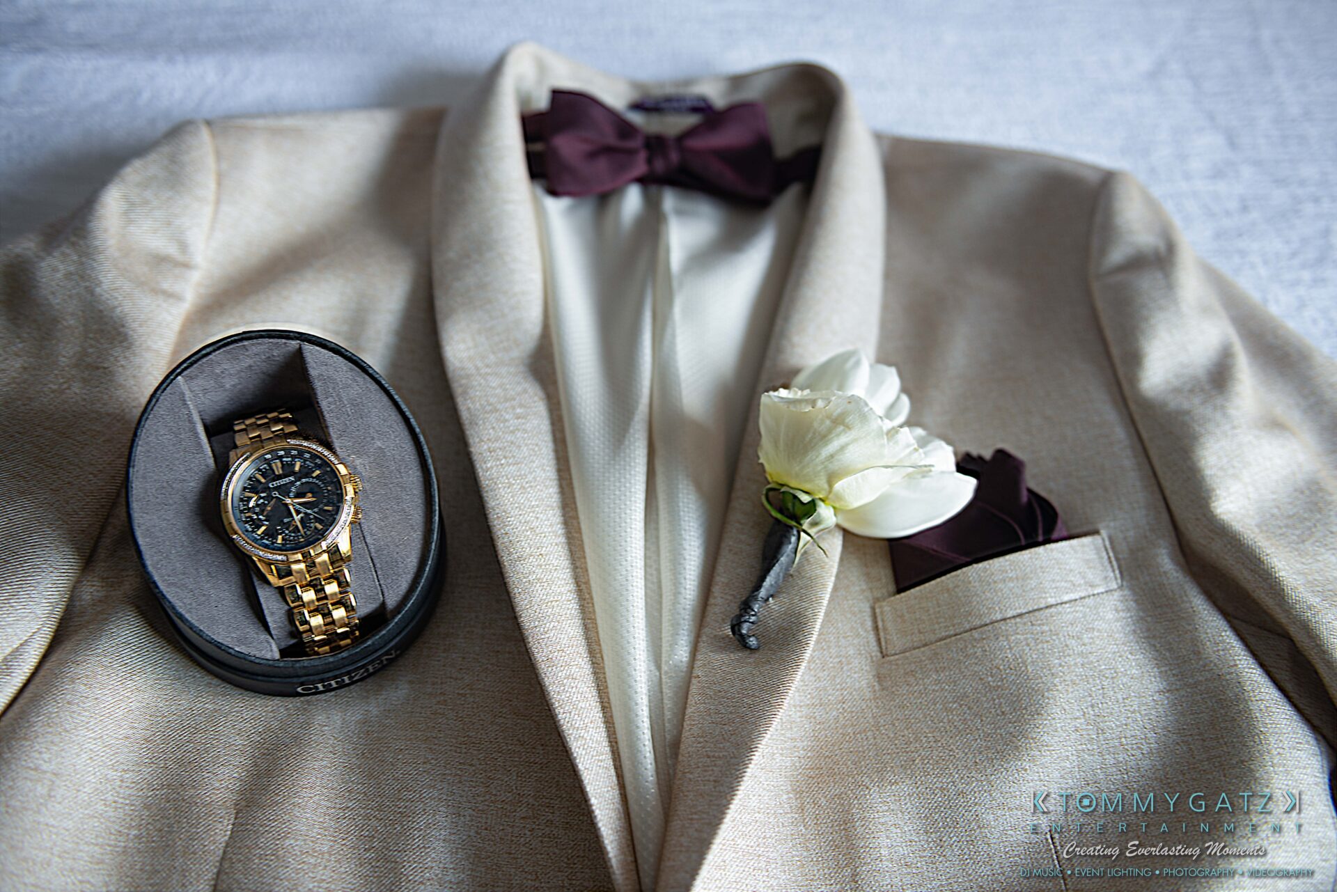 Harris-Wedding-HIGHLIGHTS-090119-35 - TOMMY GATZ ENTERTAINMENT A beige suit with a burgundy bow tie, a white boutonniere in the pocket, and a gold wristwatch in a black box placed on the suit.