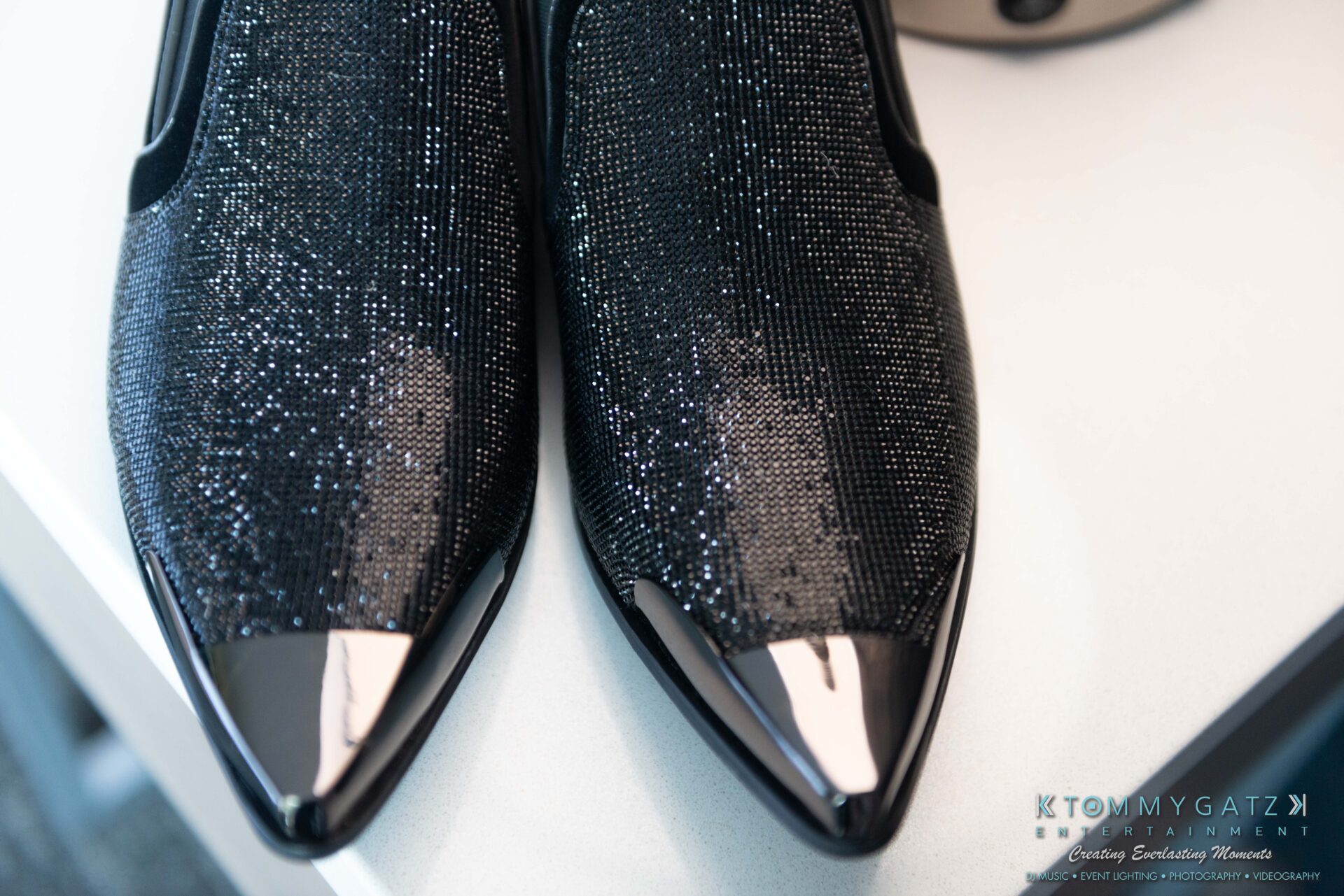 Harris-Wedding-HIGHLIGHTS-090119-36 - TOMMY GATZ ENTERTAINMENT Close-up of black glittery shoes with glossy pointed tips on a table surface.
