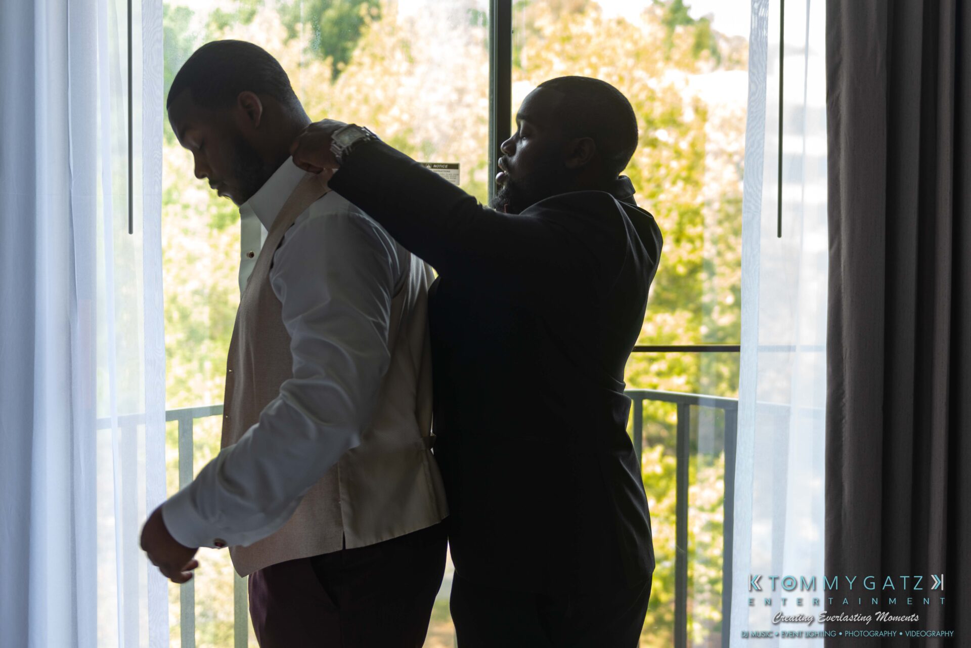 Harris-Wedding-HIGHLIGHTS-090119-39 - TOMMY GATZ ENTERTAINMENT Two men in formal attire by a window; one adjusts the other's vest and collar inside a well-lit room.
