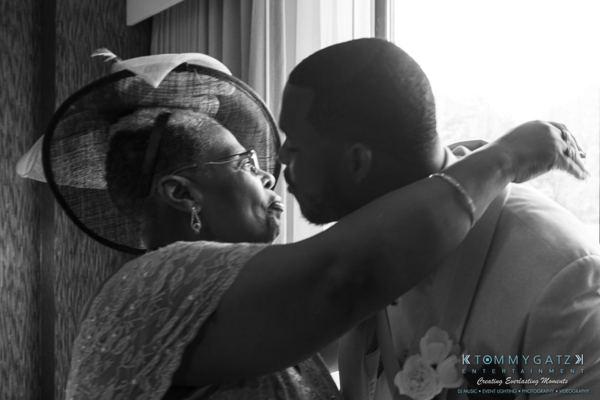 Harris-Wedding-HIGHLIGHTS-090119-46 - TOMMY GATZ ENTERTAINMENT A woman and a man share an affectionate moment near a window. The woman wears a hat, and the man is dressed in a suit.