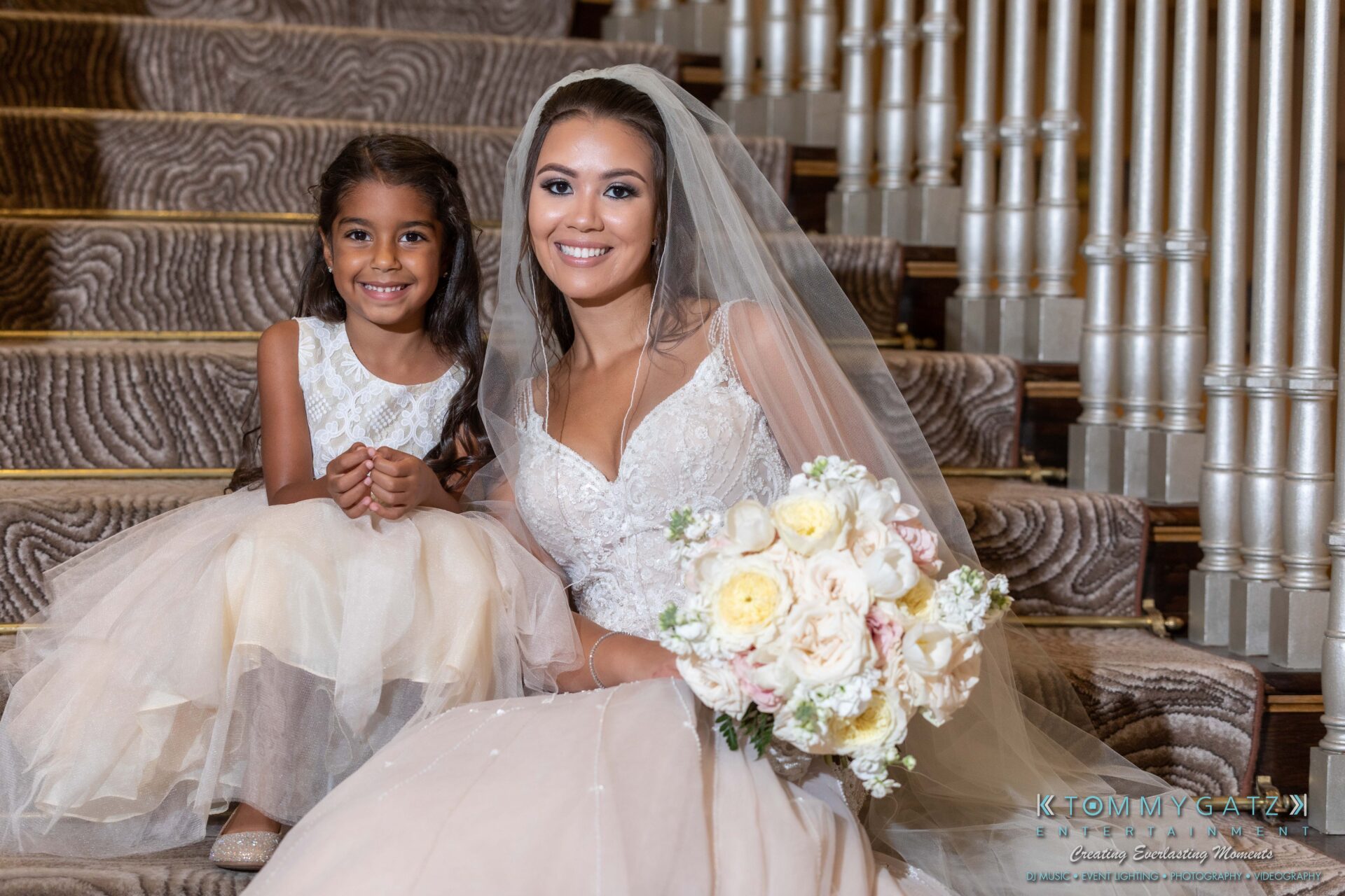 Harris-Wedding-HIGHLIGHTS-090119-49 - TOMMY GATZ ENTERTAINMENT Bride in a white gown holding a bouquet, sitting on stairs next to a young girl in a dress.