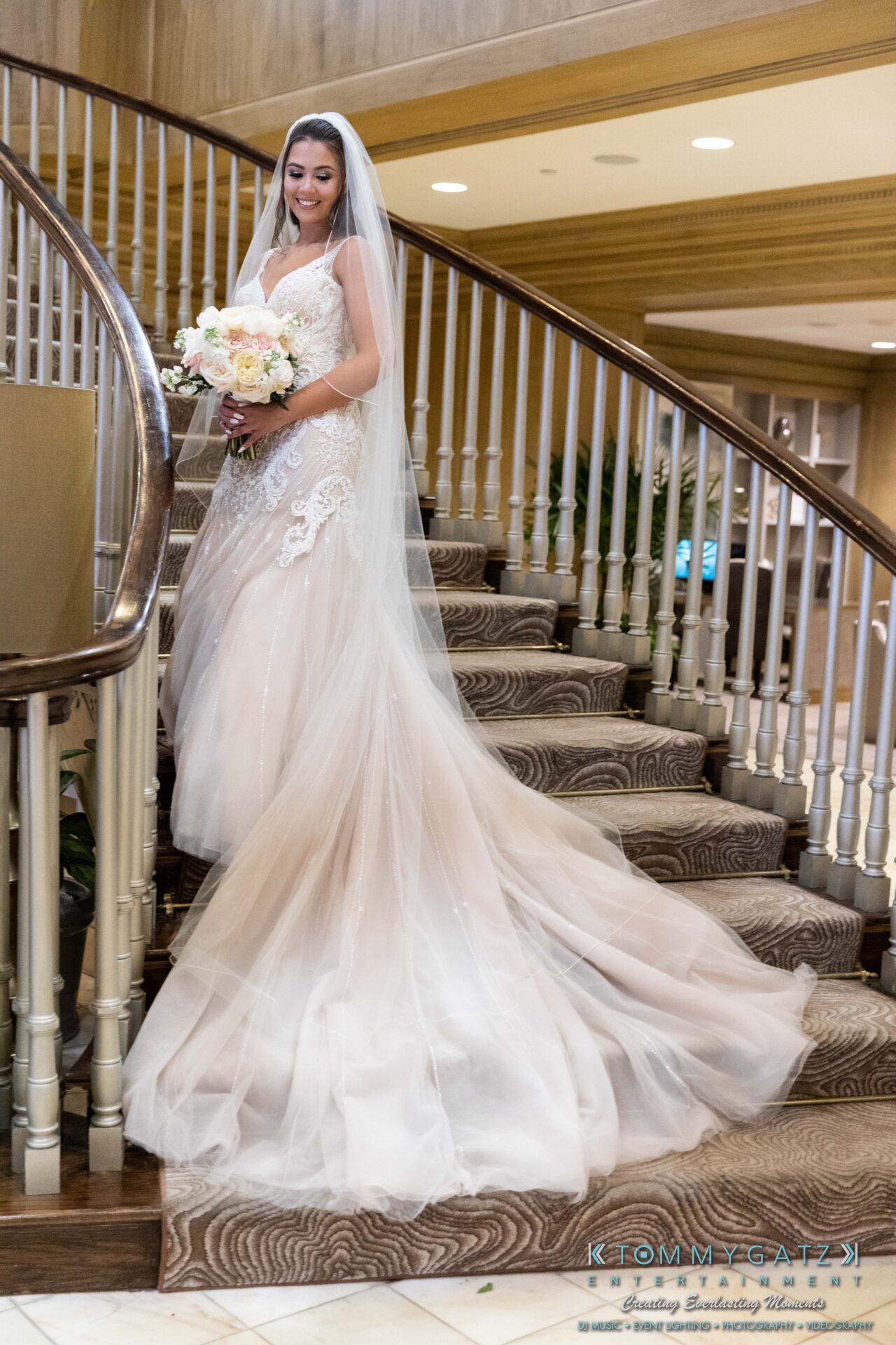 Harris-Wedding-HIGHLIGHTS-090119-52 - TOMMY GATZ ENTERTAINMENT Bride in a lace wedding gown and veil descends a carpeted staircase, holding a bouquet of flowers.