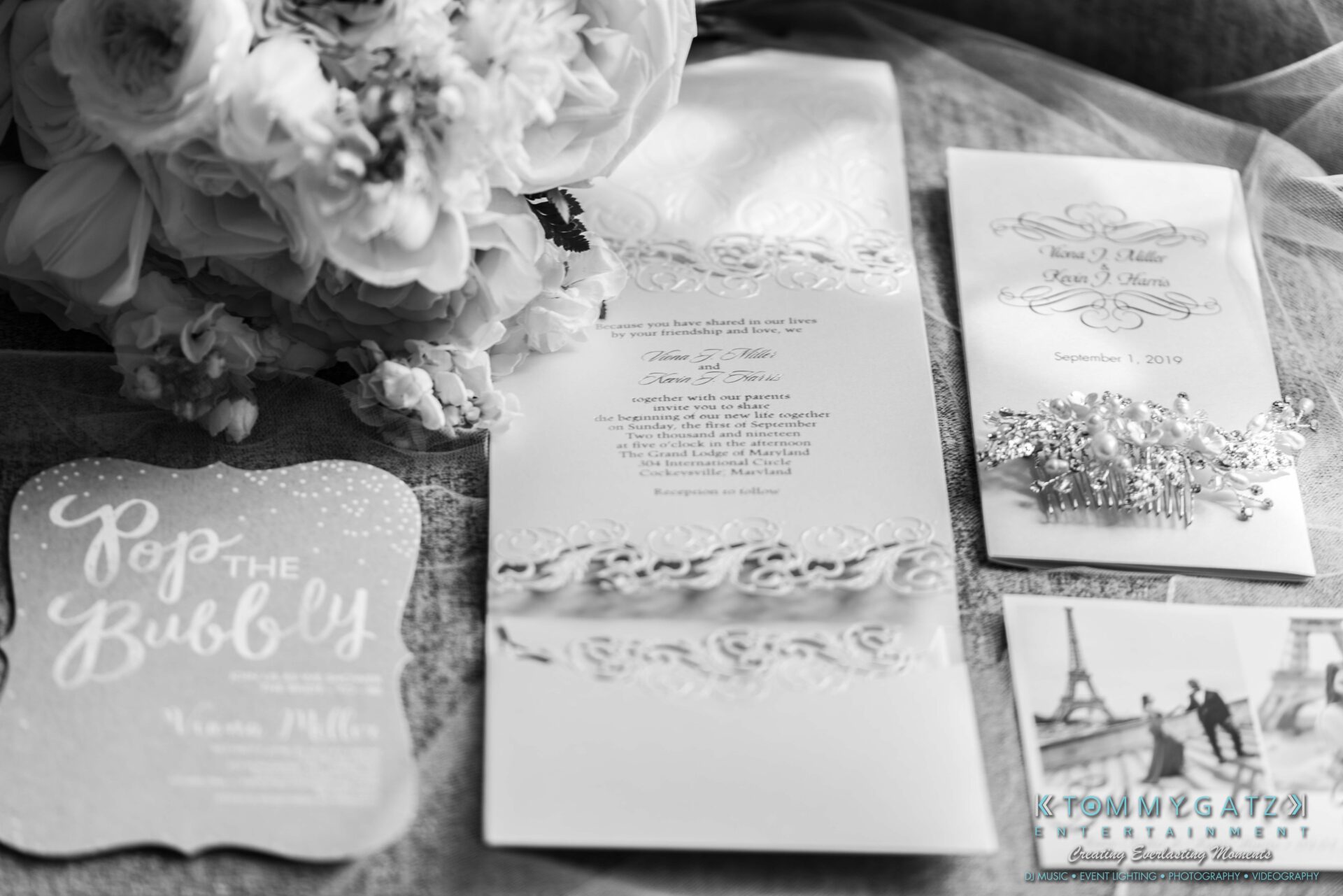A black and white image of wedding stationery and decorations, including invitations, a floral arrangement, and a decorative card reading "Pop the Bubbly.