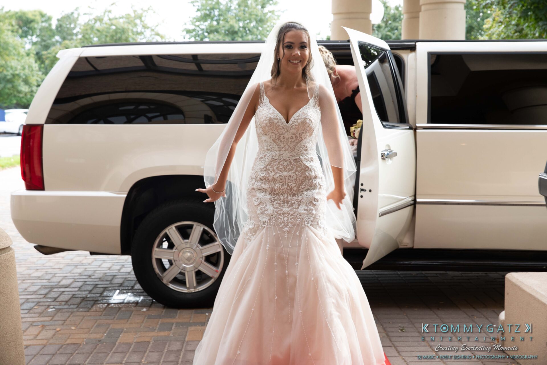 Harris-Wedding-HIGHLIGHTS-090119-62 - TOMMY GATZ ENTERTAINMENT Bride in a detailed lace gown steps out of a white limousine, smiling.
