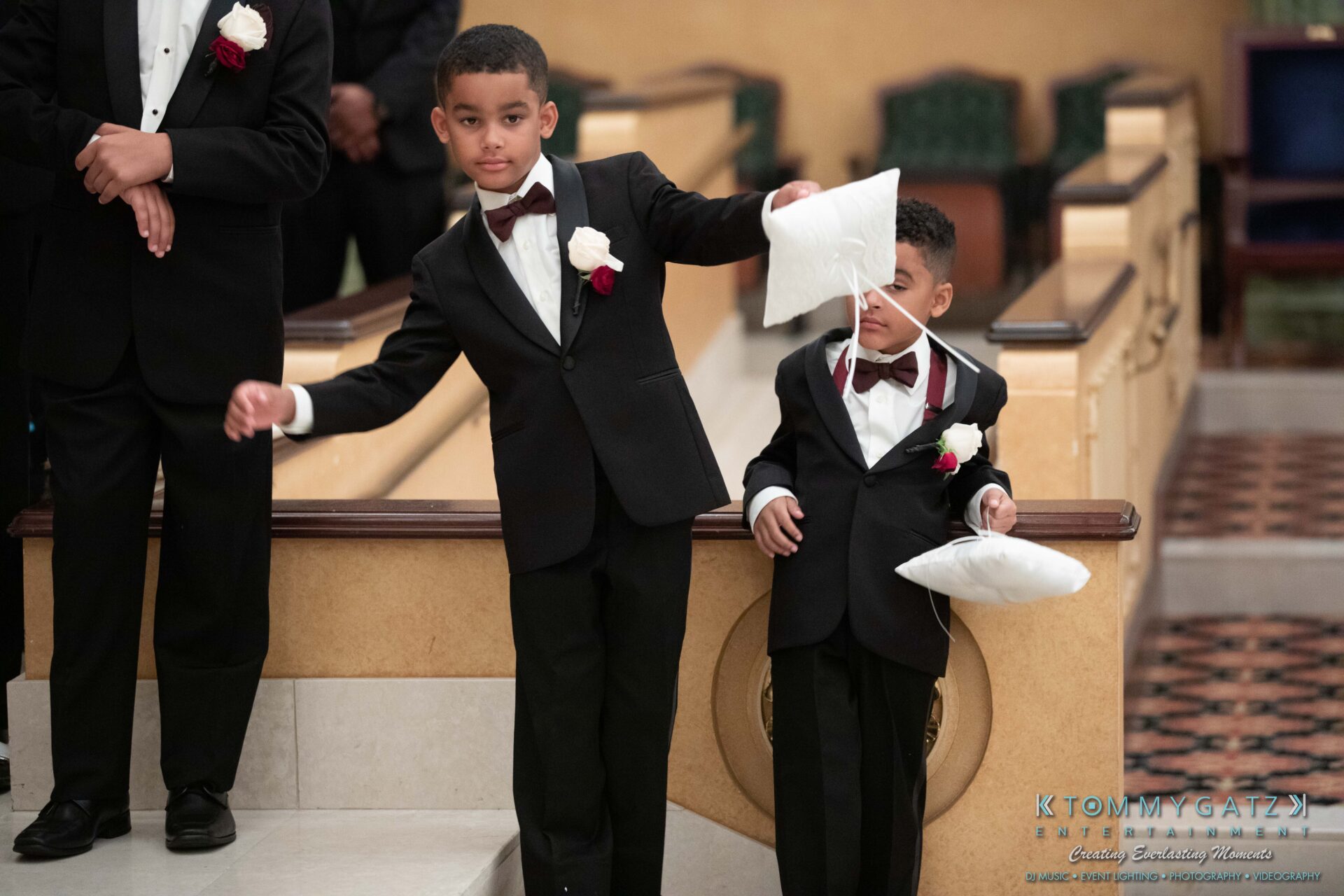 Harris-Wedding-HIGHLIGHTS-090119-82 - TOMMY GATZ ENTERTAINMENT Two young boys in suits, one holding a pillow and the other with a pillow tucked under his arm, stand at the edge of a staircase during an indoor event.