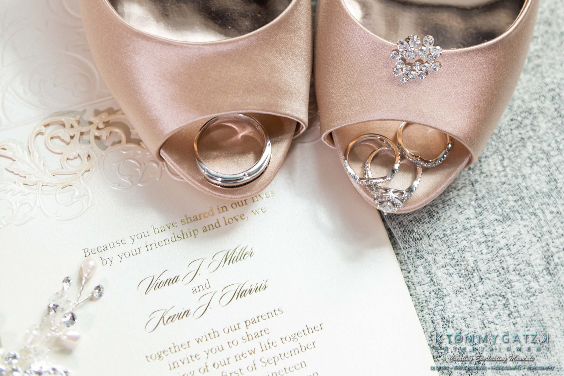 Harris-Wedding-HIGHLIGHTS-090119-9 - TOMMY GATZ ENTERTAINMENT Wedding invitation with embossed details next to two champagne-colored heels adorned with jewelry and two rings.