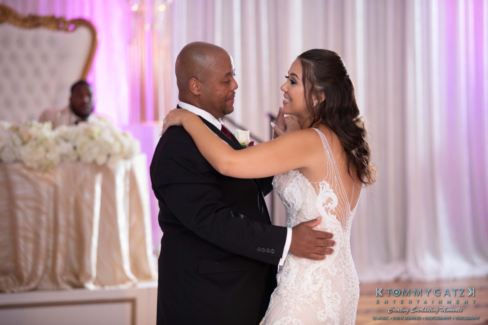 Harris-Wedding-HIGHLIGHTS-090119-96 - TOMMY GATZ ENTERTAINMENT A bride and a man dance together on a ballroom floor, with a white and pink decor backdrop.