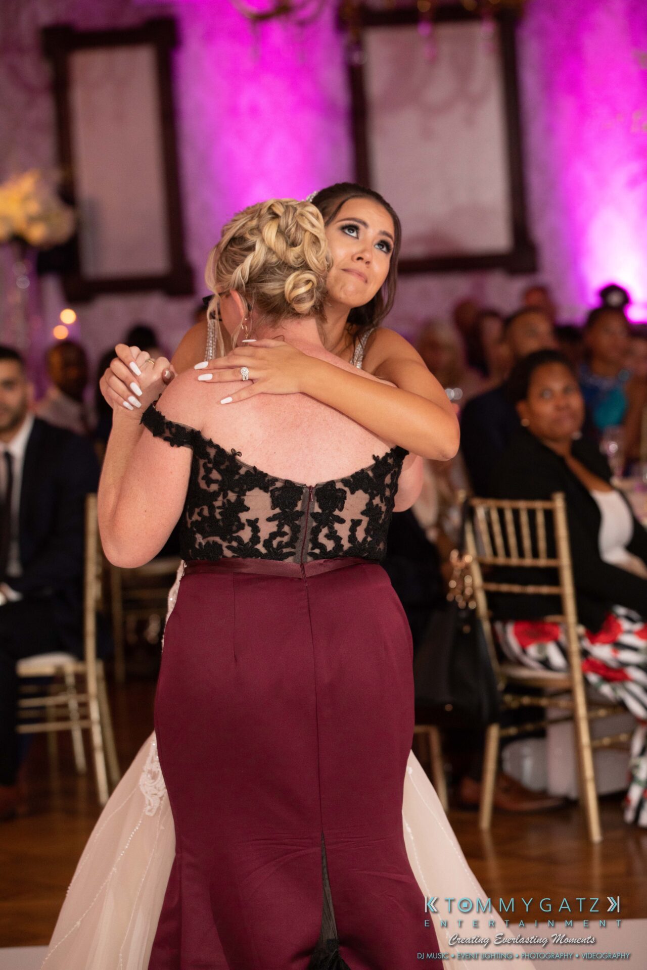 Harris-Wedding-HIGHLIGHTS-090119-98 - TOMMY GATZ ENTERTAINMENT A bride and a woman embrace on a dance floor during a formal event, with guests seated in the background.