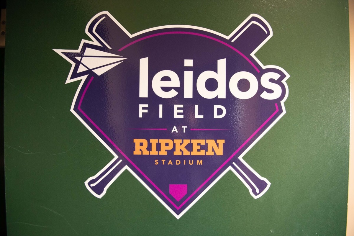 Heather-Scott-Wedding-Low-Res-1 1 - TOMMY GATZ ENTERTAINMENT Leidos Field logo at Ripken Stadium featuring baseball bats and a diamond shape over a green background.