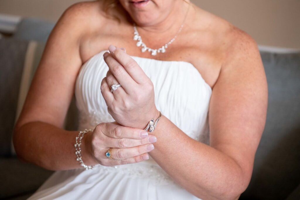 Heather-Scott-Wedding-Low-Res-10 1 - TOMMY GATZ ENTERTAINMENT A person in a white strapless dress adjusts a bracelet on their wrist. They are also wearing a ring and a necklace.