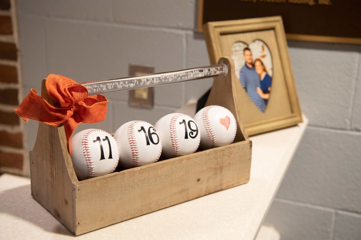 Heather-Scott-Wedding-Low-Res-130 1 - TOMMY GATZ ENTERTAINMENT A wooden crate holds four baseballs with the numbers 11, 16, and 19, and a heart symbol. A photo in a frame is in the background.